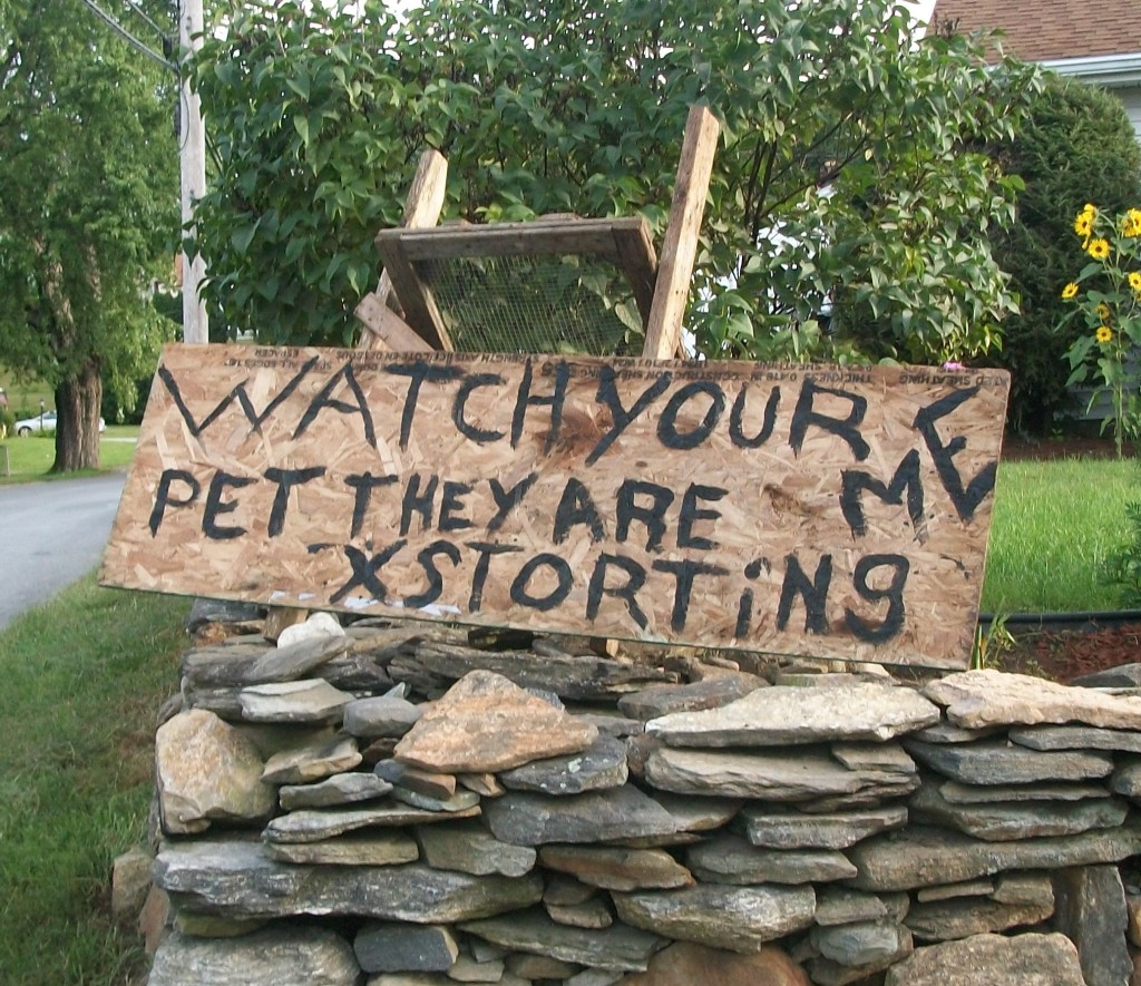 handwritten lawn sign on particle board that says WATCH YOUR PET THEY ARE XTORTING ME